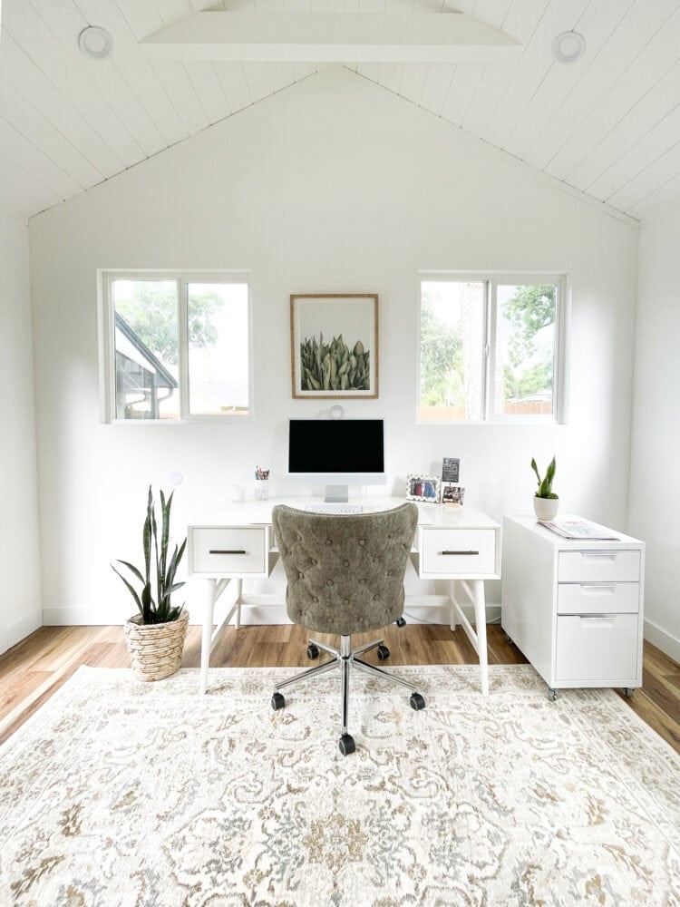 Inside she shed office with white desk, green chair, and computer.