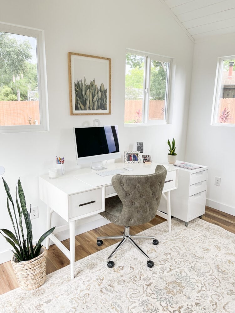 Inside she shed office with white desk, green chair, and computer.