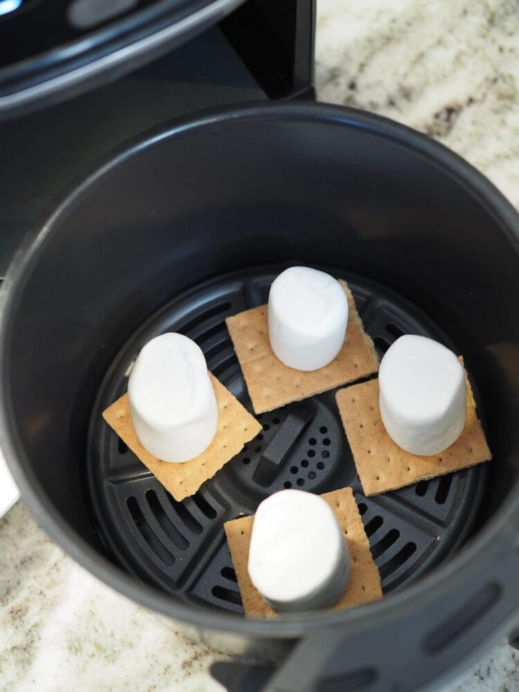 Looking inside an air fryer basket at four graham crackers with a large marshmallow on each.