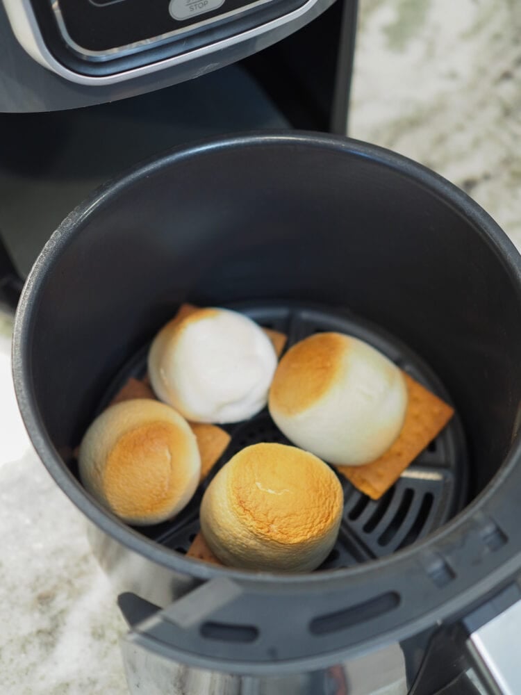 A look inside an air fryer basked with four large marshmallows tan and toasted on top of graham crackers.