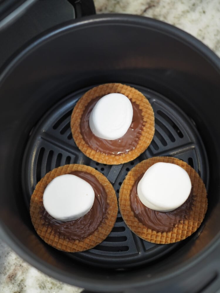 Three stroopwaffels with nutella and a marshmallow inside an air fryer basket.