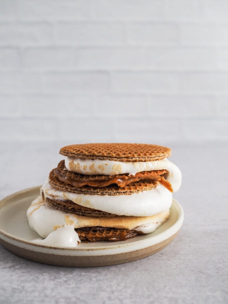 Side angle view showing three stroopwaffel s'mores stacked on a plate with melty marshmallow poofing out over the sides.