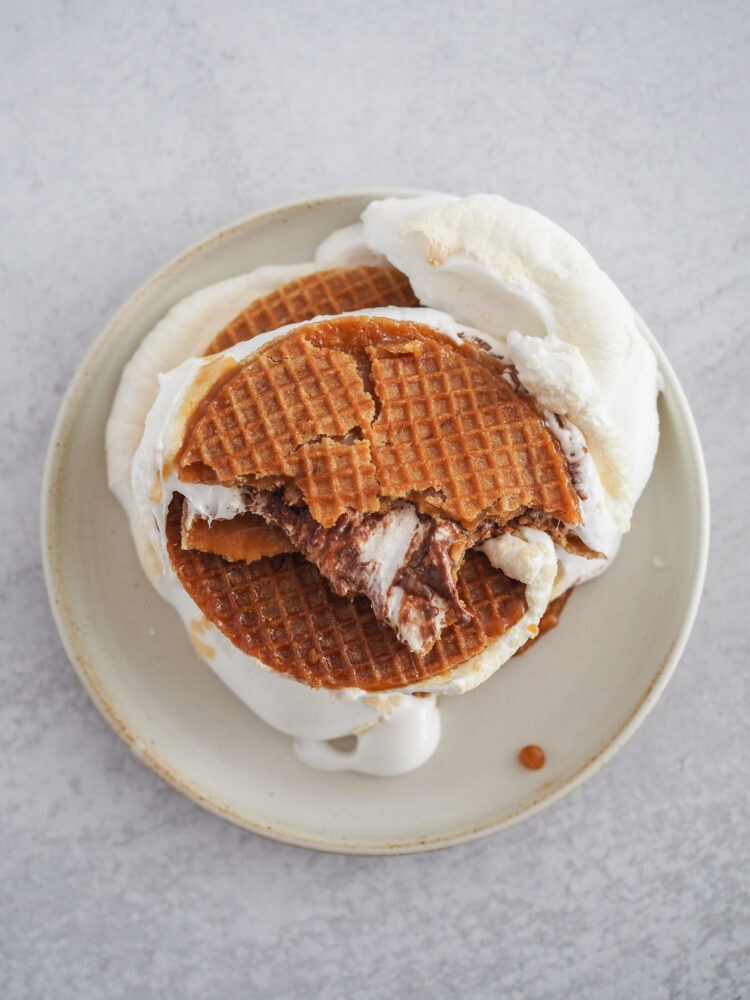 Overhead look at stroopwaffel smores stacked on a plate with the top one torn in half showing the melty marshmallow and Nutella center.