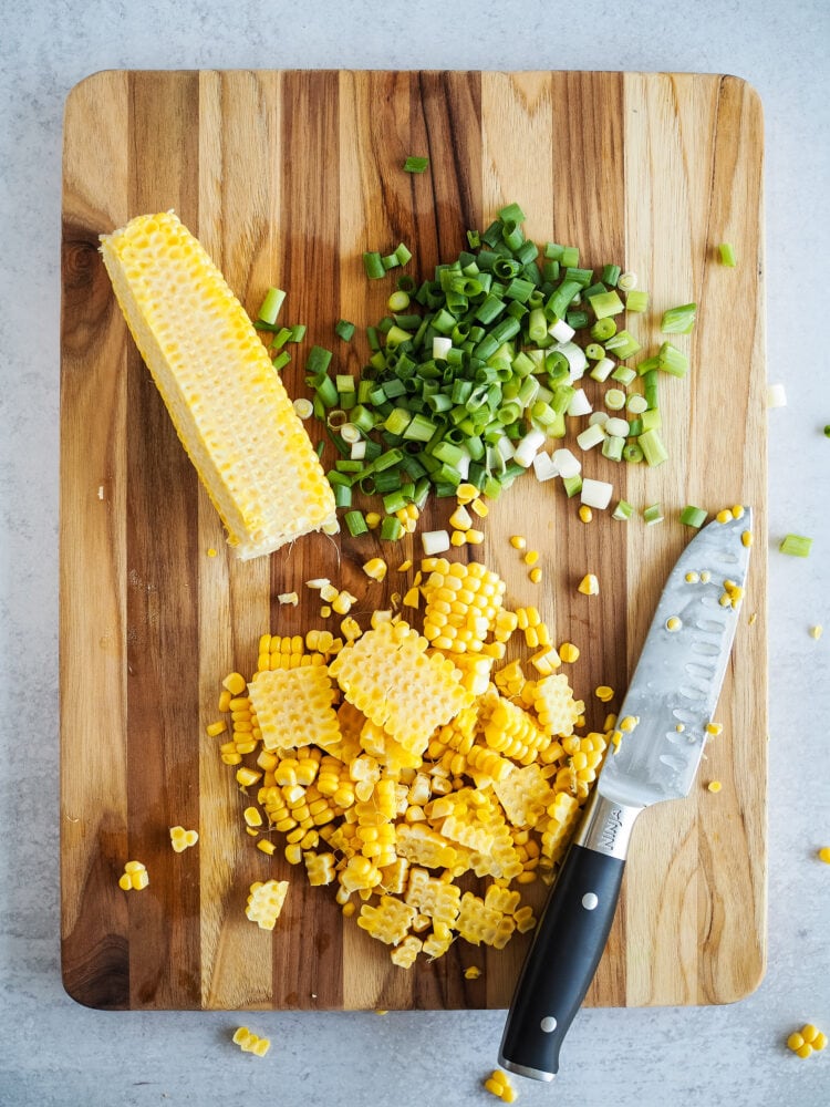 Wood cutting board with diced green onion and corn cut from the cob.