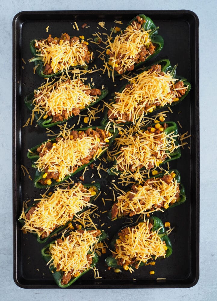 Poblano peppers on baking sheet, filled with stuffing and topped with cheese.