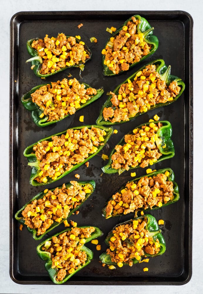 Poblano peppers on a baking sheet stuffed with chorizo and corn.