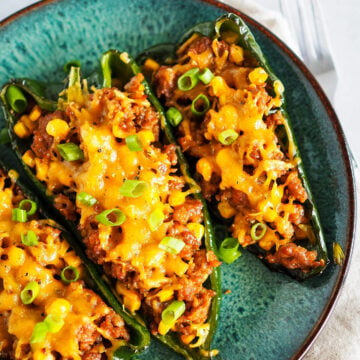 Blue plate with three chorizo stuffed poblano peppers topped with melted cheese.