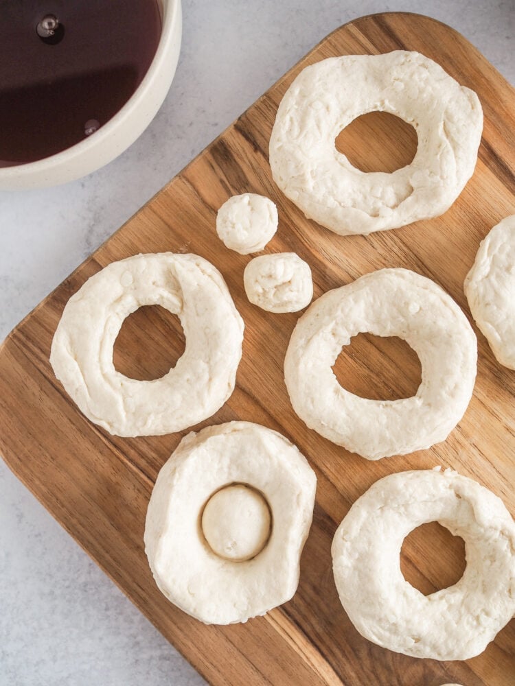 Wood cutting board with raw biscuit dough forming donut shapes with holes cut into the middle.