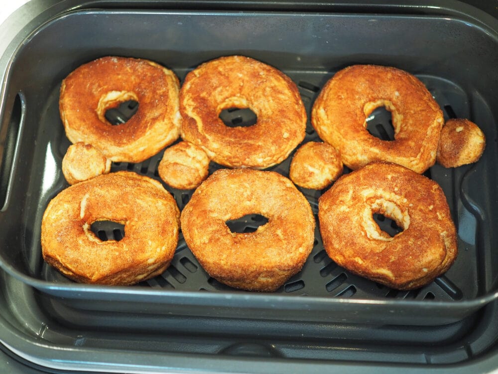 Six air fried donuts in an air fryer basket.