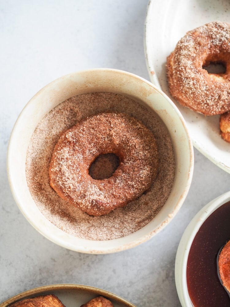 Close up of air fried donut in bowl of cinnamon sugar.