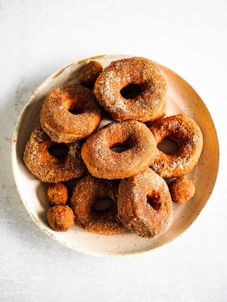 Overhead photo looking down at a large ceramic plate of golden brown air fried donuts and donut holes dusted in cinnamon sugar.