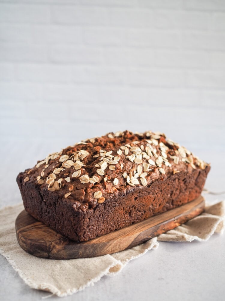 A loaf of fresh baked Irish brown bread on a wood board resting on a natural linen cloth in a white kitchen.