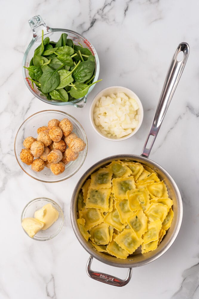 Ingredients for ravioli and meatball skillet including spinach, diced onion, meatballs, butter, and ravioli.