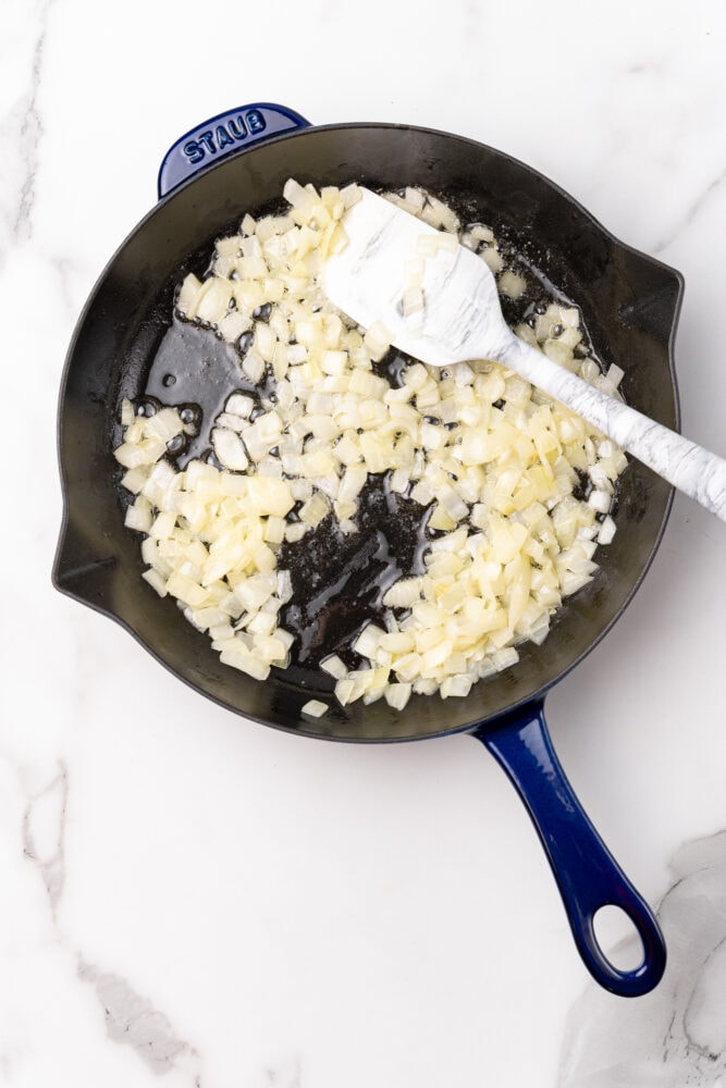 Blue Staub skillet with diced onions cooking in butter.