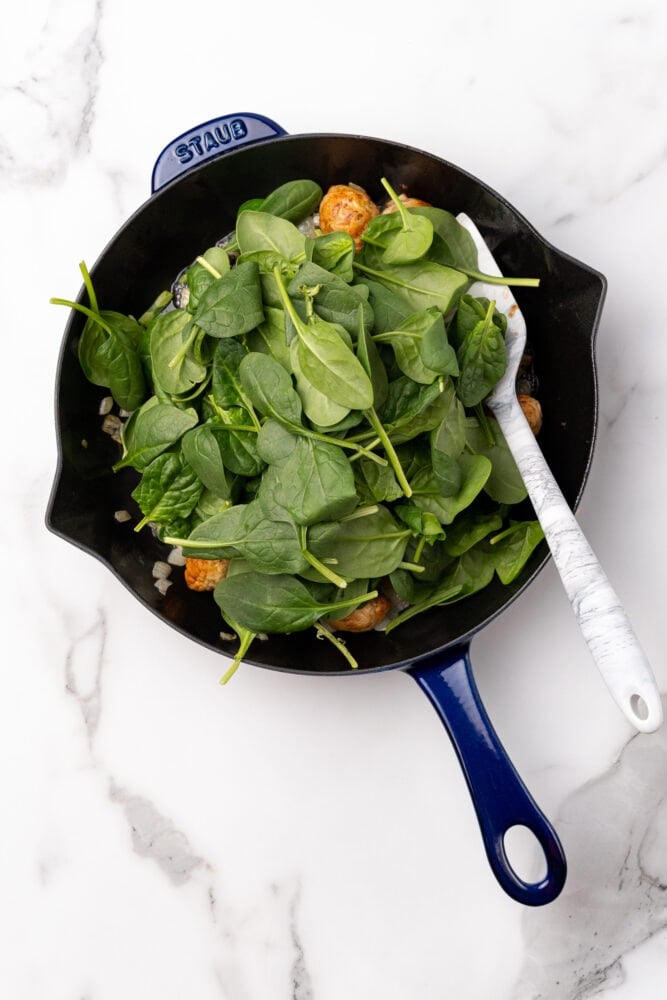 Blue Staub skillet with fresh spinach added on top of meatballs and onion.