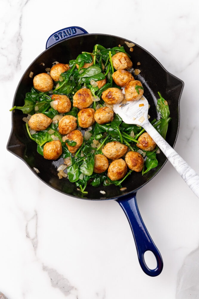 Blue Staub skillet with sautéed meatballs, spinach, and onion.