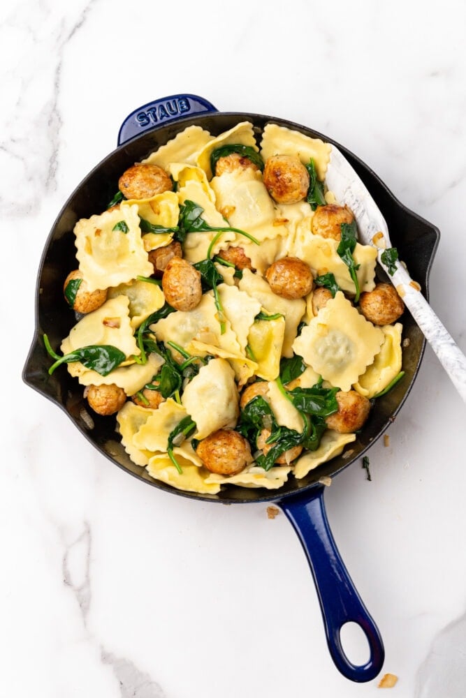 Blue Staub skillet with ravioli, spinach and meatballs.