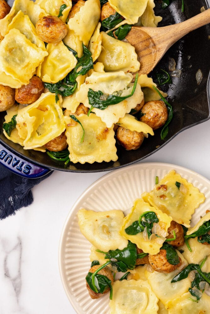 Overhead look of ravioli and meatballs ready to serve with a wooden spoon. There's a plate of ravioli and meatballs to the side.