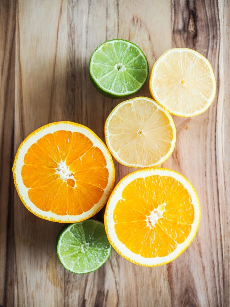 Orange, lime, and lemon sliced in half on a wood cutting board.