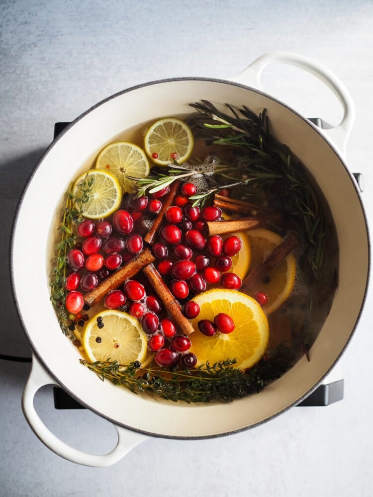 A holiday simmer pot filled with cranberries, cinnamon sticks, fresh cut citrus and herbs