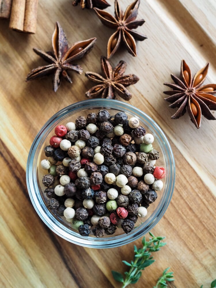 glass bowl of peppercorns on a wood cutting dish with star anise and thyme on the side