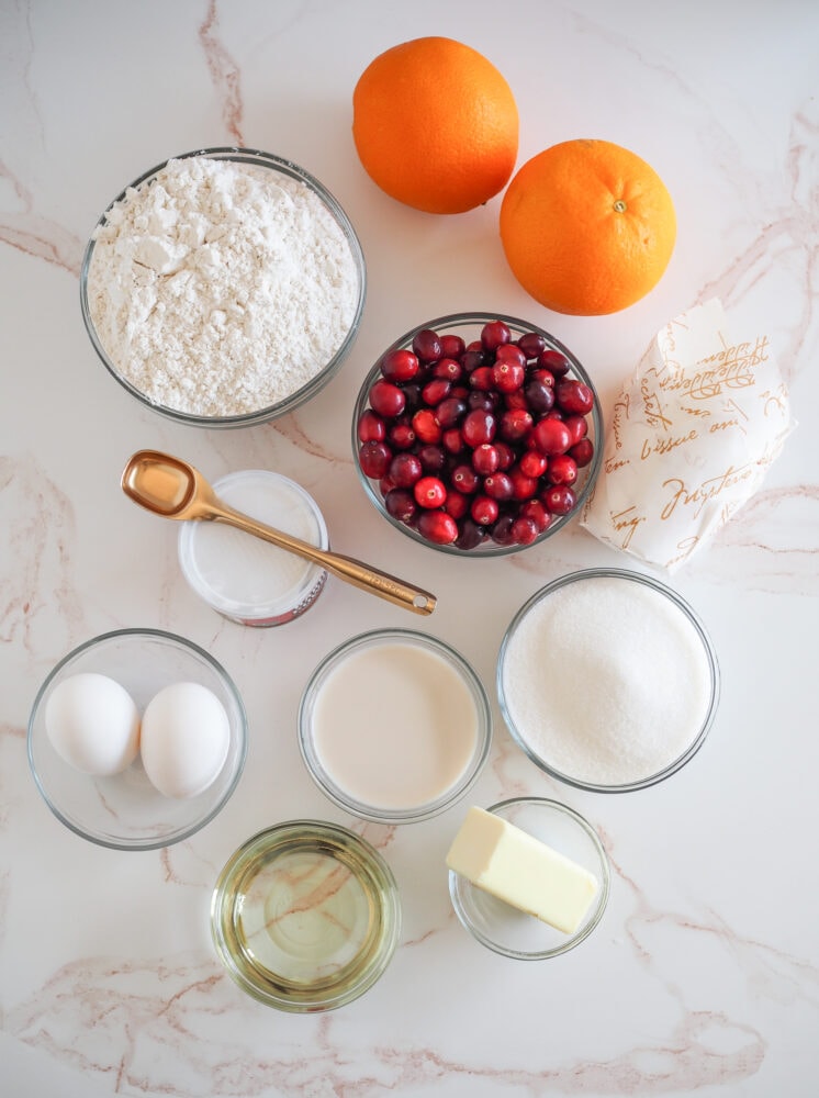 Ingredients for Cranberry Orange Muffins including flour, cranberries, oranges, eggs, milk, baking powder, sugar, oil, and butter.