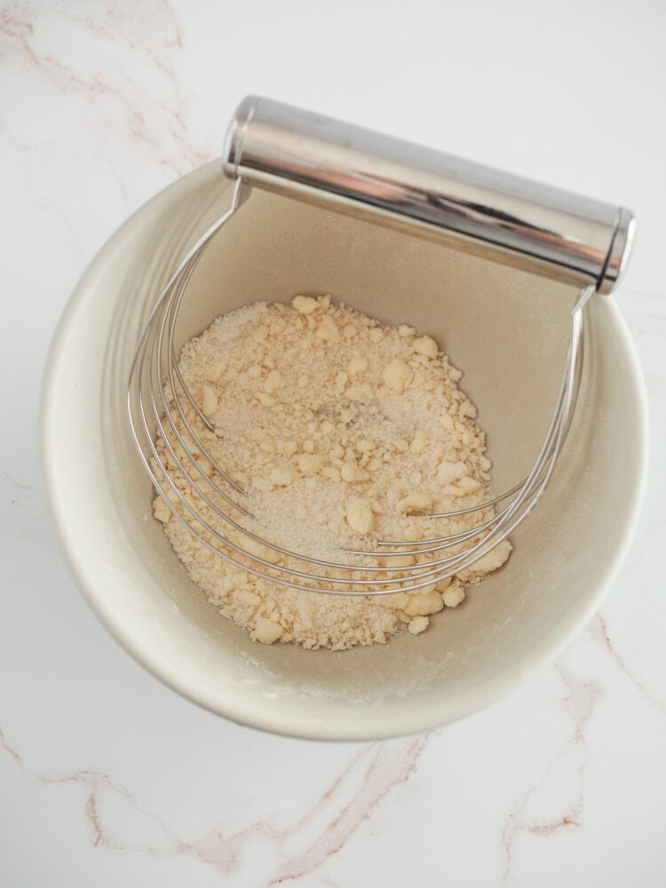 Flour, butter, and sugar in a bowl with a pastry cutter getting pressed into a crumb topping.