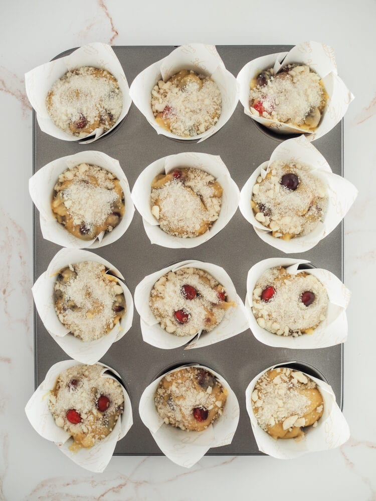 muffin batter with crumb topping in paper tulip cups sitting in muffin tin before baking