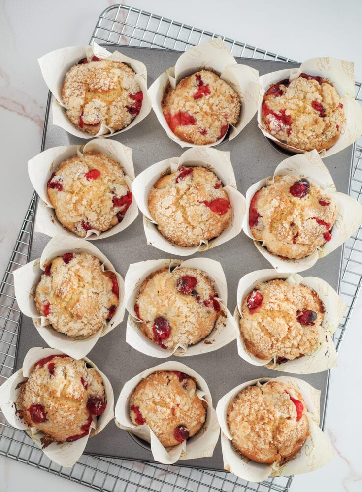 baked cranberry orange muffins in muffin tin resting on cooling rack