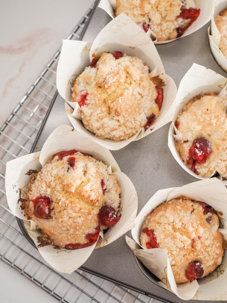 Cranberry orange muffins in paper tulip cups in a muffin tin cooling on a cooling rack.