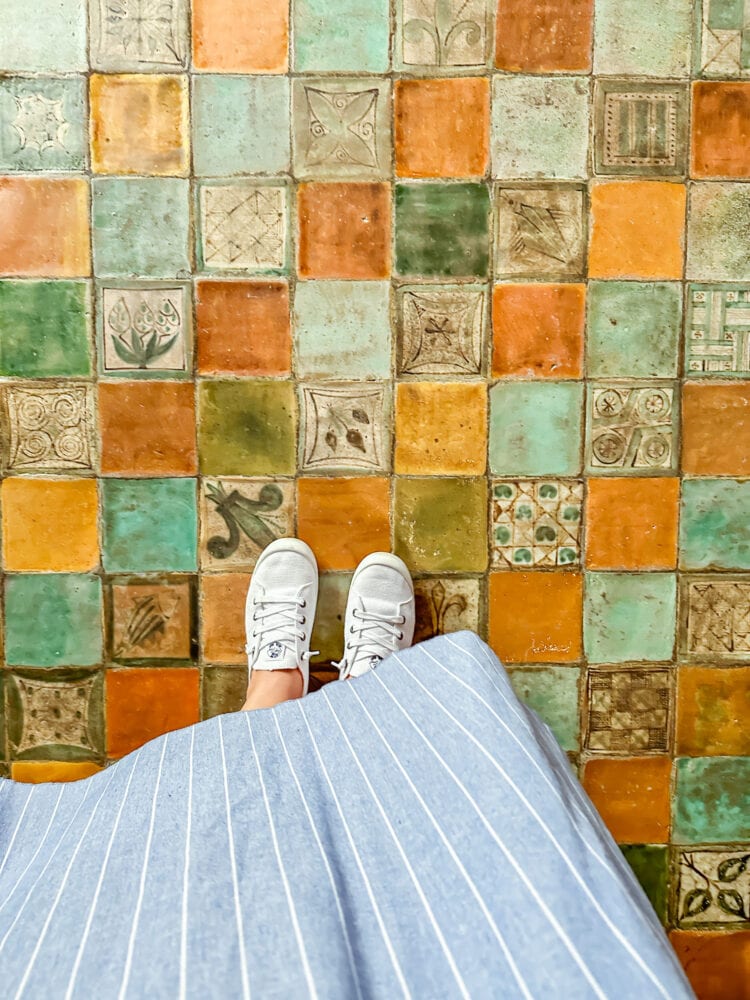 Colorful tile floor, with terracotta, green, gold, and teal colored tiles. Some have designs such as a fleur de lis, or hearts, or leaves. And some are solid colors.