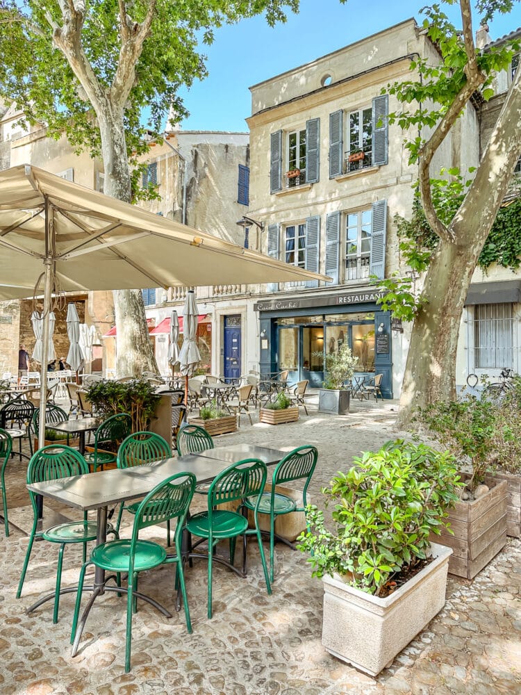 Outdoor dining with green chairs and a white umbrella in a town square in Avignon.