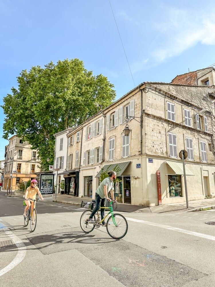 Two people riding bikes down a street in Avignon, France.
