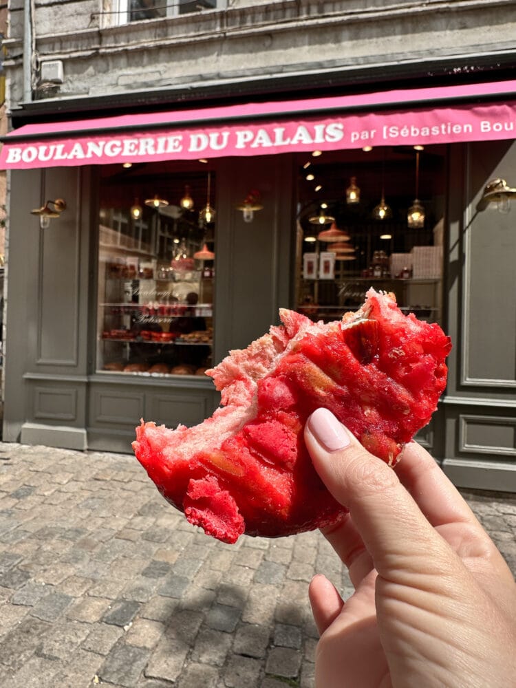 Rachelle holding a torn piece of the pink brioches aux pralines roses outside of Boulangerie Du Palais in Lyon.