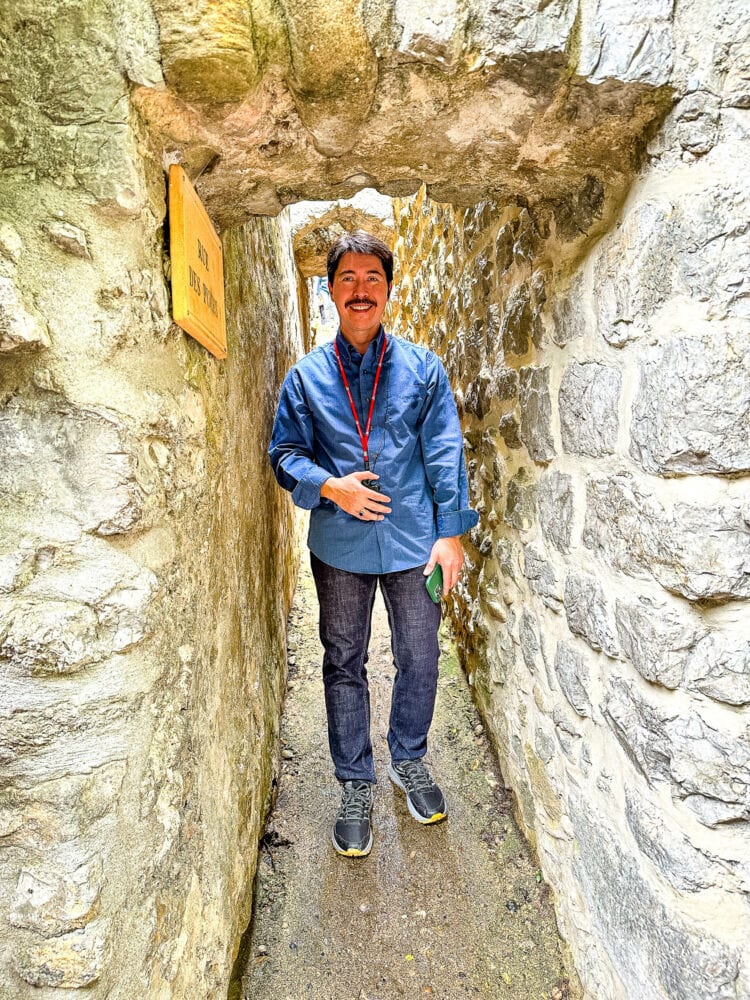 Pete walking through a narrow passageway in between stone walls in the village of Vogüé, France.