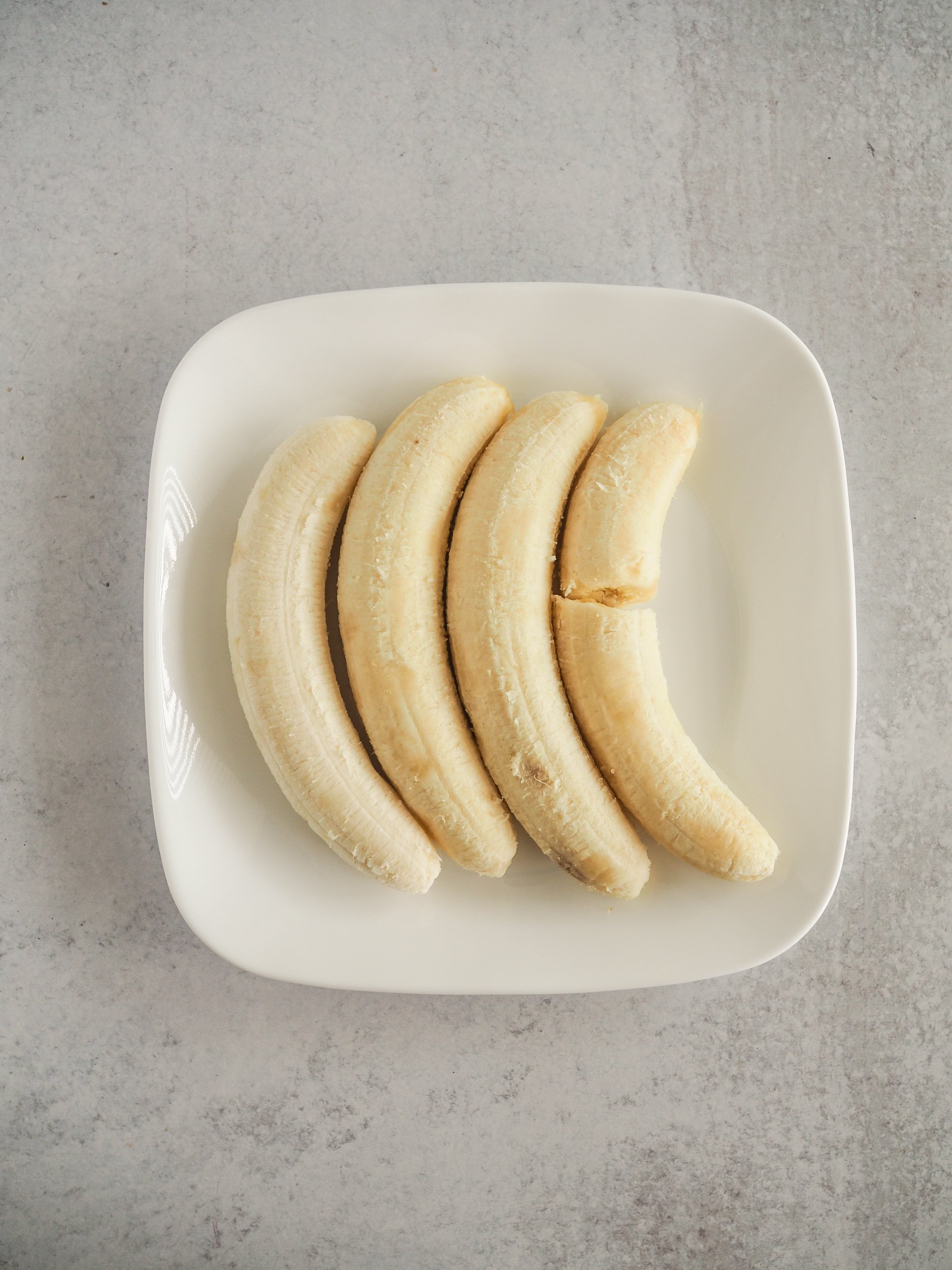 Four bananas on a white plate before getting mashed.
