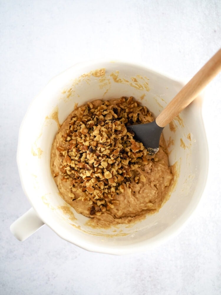 Walnuts added to banana nut muffin batter in small mixing bowl.