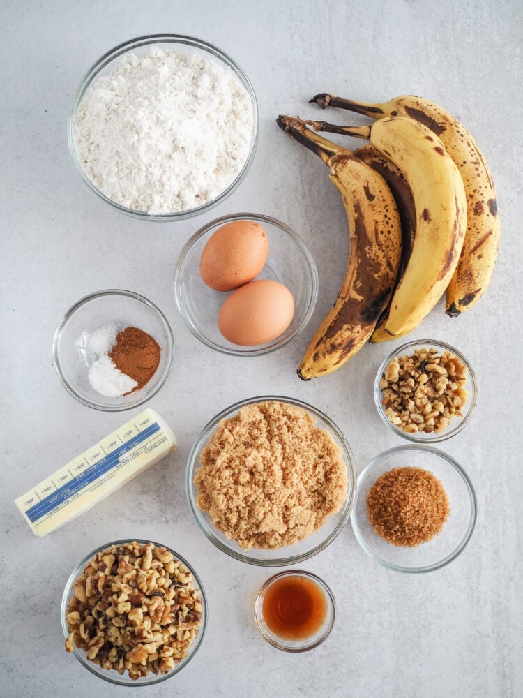 Ingredients for banana nut muffins including bananas, flour, eggs, spices, butter, brown sugar, walnuts, vanilla, and turbinado sugar.