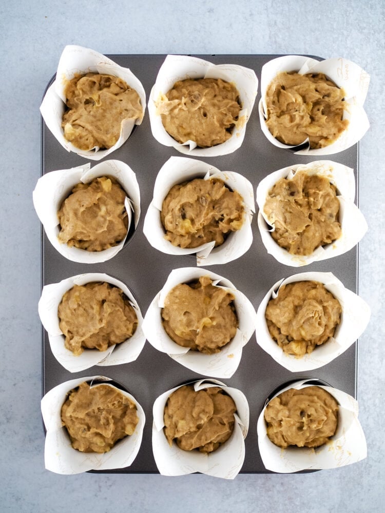 Banana nut muffins batter in paper cups in a 12 muffin muffin tin before being baked.