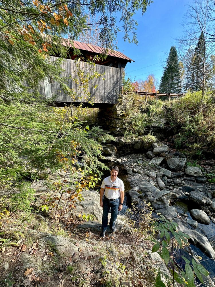 Pete standing by a river with a covered bridge in the background