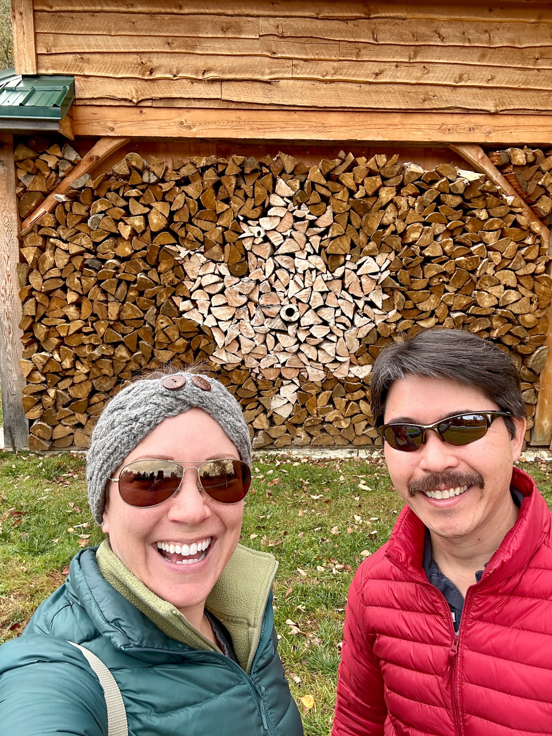 Rachelle and Pete standing in front of a pile of wood arranged to look like a maple leaf.