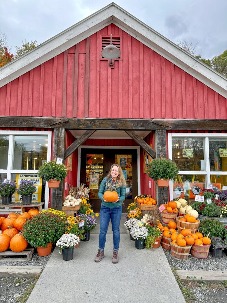 Rachelle standing outside a contry store holding a pumpkin.