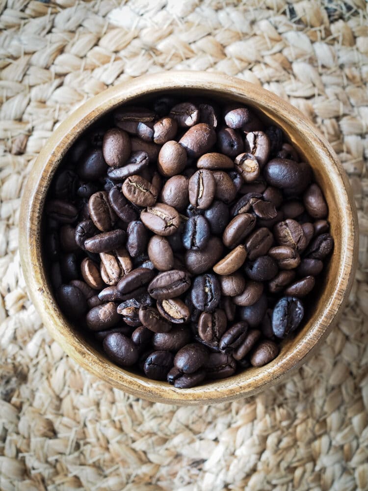 A mix of light and dark coffee beans in a wood bowl