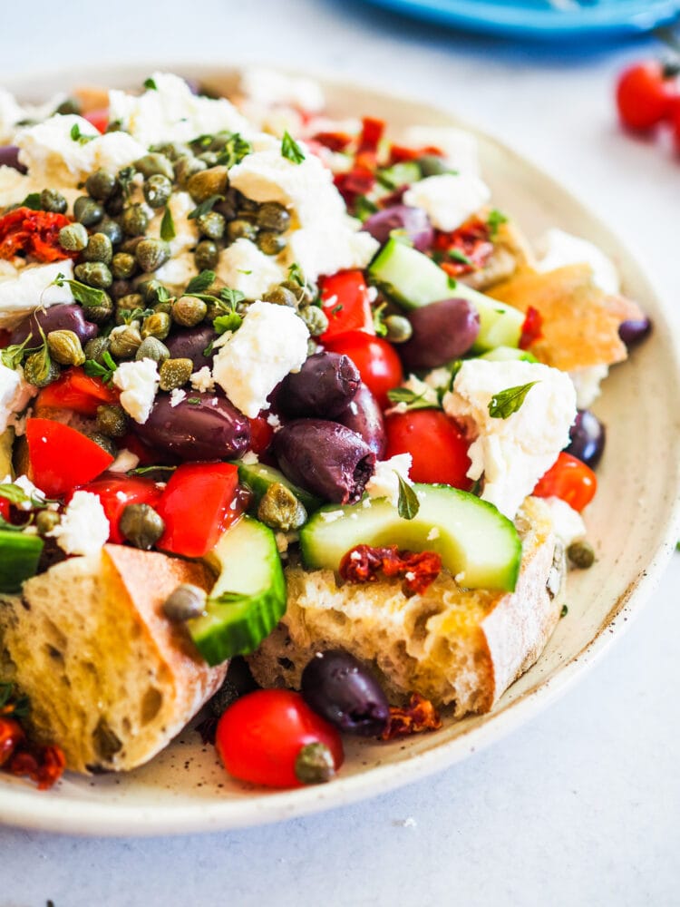 Side view of dakos salad including crusty bread, tomatoes, cucumbers, capers, kalamata olives, feta, and oregano.