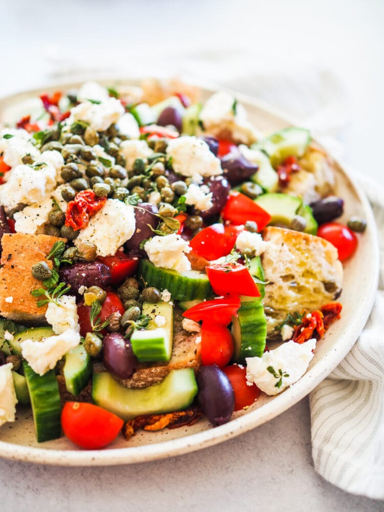 Dakos salad including crusty bread, cucumber, tomatoes, sun dried tomatoes, kalamata olives, capers, oregano, and olive oil and red wine vinegar.