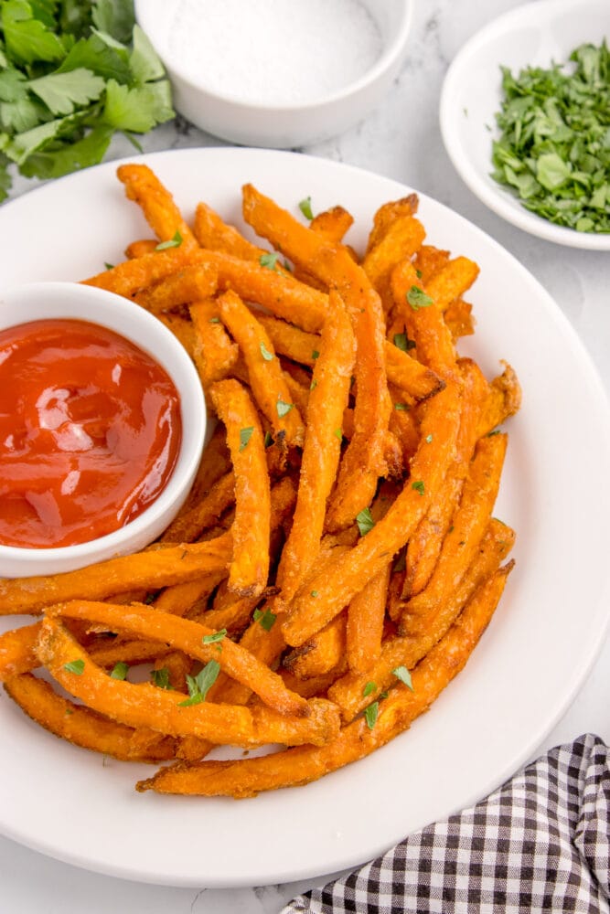 white bowl with air fried frozen sweet potato fries, garnished with parsley, and a side of ketchup