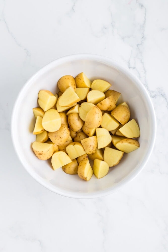 raw potatoes, cut into halves and quarter, in a white bowl