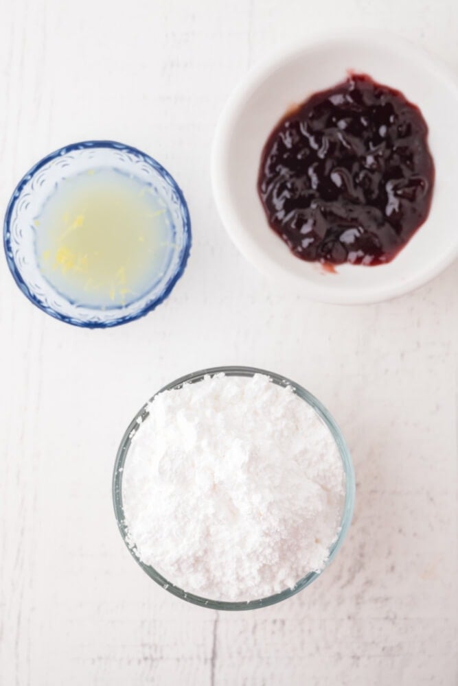 Ingredients to make raspberry glaze including raspberry jam, lemon juice and zest, and powdered sugar
