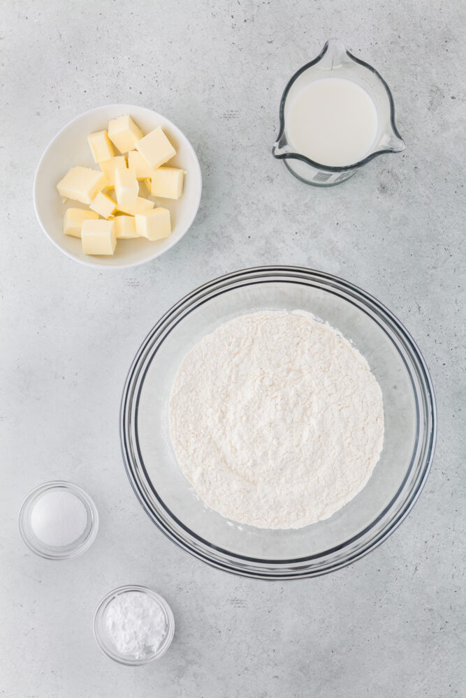 Ingredients to make biscuits in an air fryer including cold cubbed butter, flour, milk, sugar, and baking powder.
