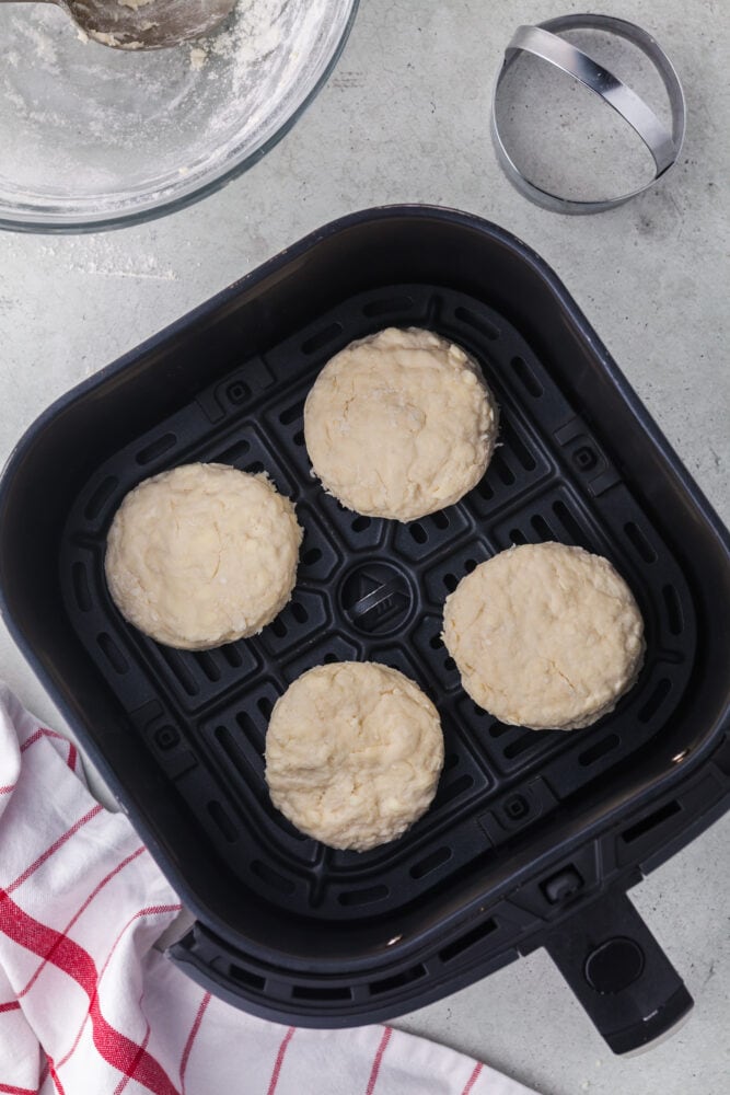 Four raw biscuits in an air fryer basket before cooking.